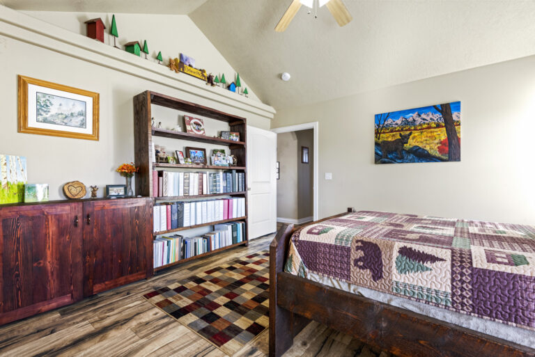 A room with books on shelves, wall frames, and a bed