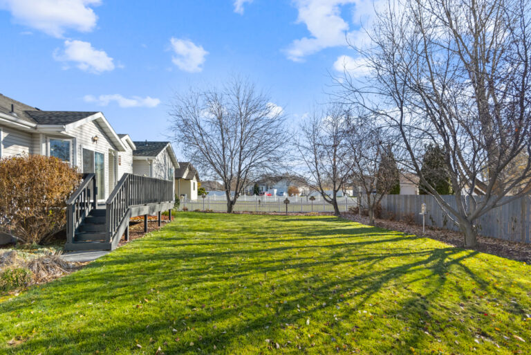 A residential home with a grassy area and tree in front, surrounded by a wooden fence